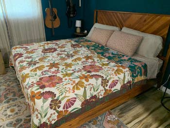 Cozy bedroom with a wooden bed featuring a floral quilt, two decorative pillows, and guitars hanging on the wall