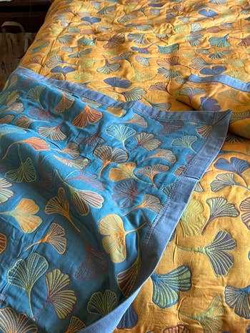 Close-up of a bedspread with a ginkgo leaf pattern on yellow and teal fabric, showcasing the bedding's elegant design and texture
