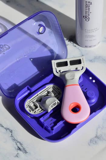 Razor kit in a purple travel case with an extra blade and shaving gel bottle, on a marble surface