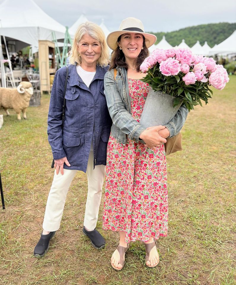 Martha Stewart standing outdoors next to another woman holding a bucket of flowers
