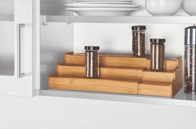 Tiered bamboo shelf organizer in a kitchen cabinet with spice jars, adding space and easy access for spices