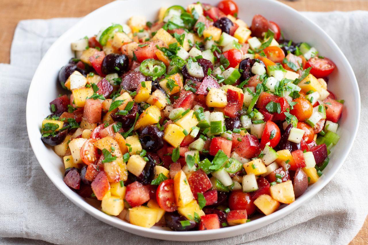 Stone fruit and vegetable salad in a serving bowl with a linen underneath.