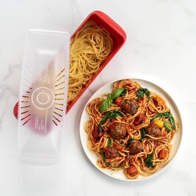Microwave pasta cooker with spaghetti and a dish of spaghetti with meatballs and vegetables nearby