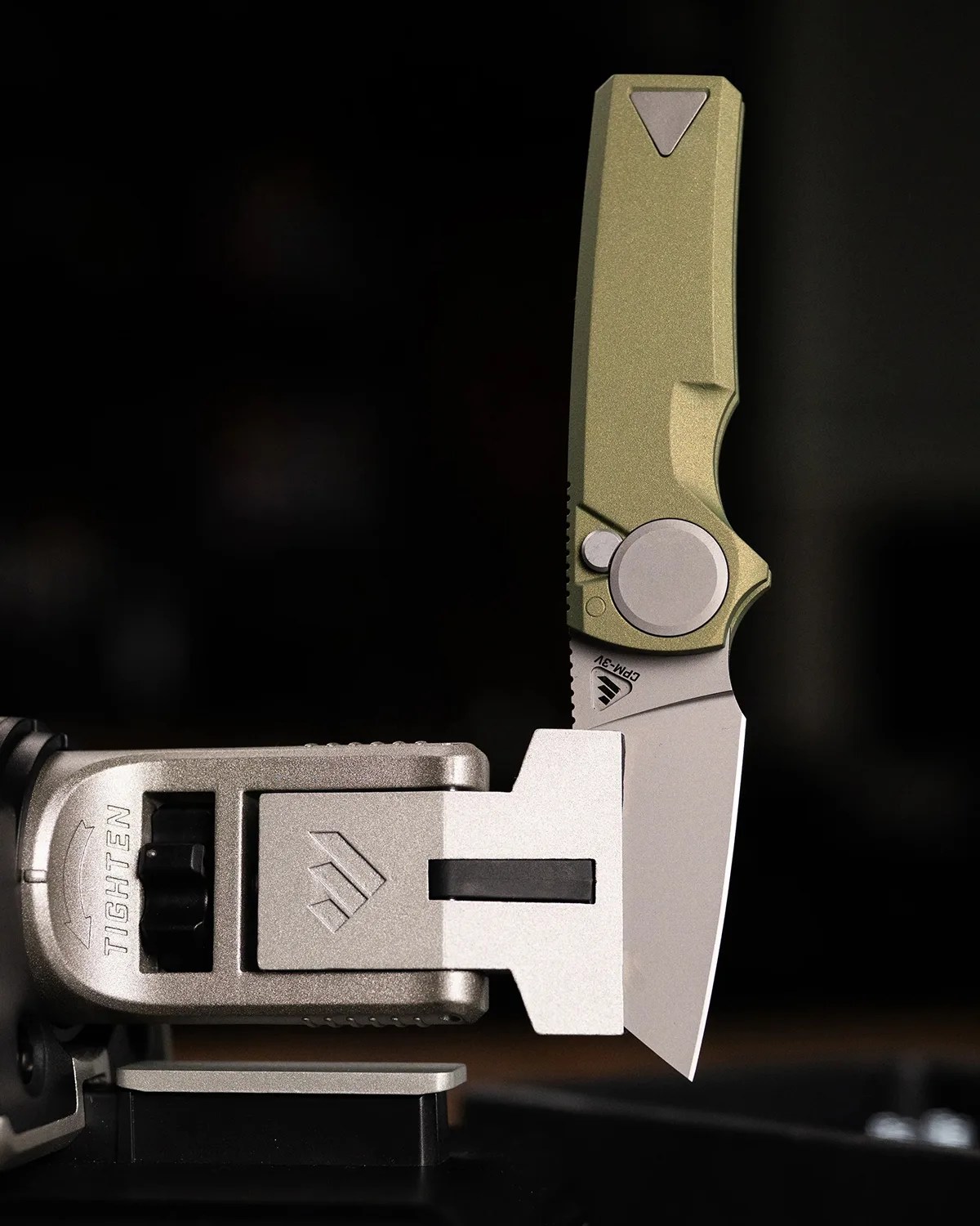 Green-handled folding knife with a silver blade clamped in a metal vise against a dark background.