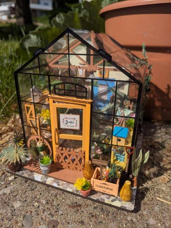 Miniature greenhouse model with intricate plants, colorful details, and gardening tools. Ideal for hobbyists and decor enthusiasts