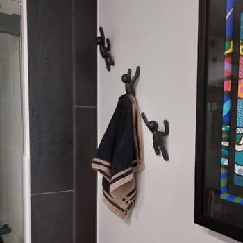 Bathroom wall with two towel hooks holding a towel and framed cartoon-style art of children with flowers