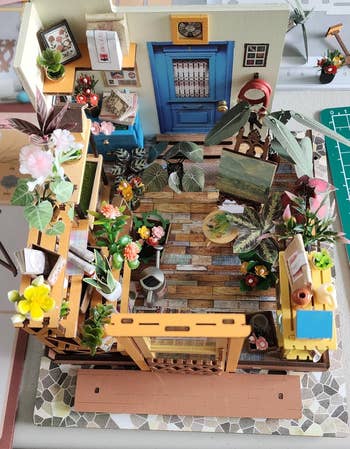 Miniature room with plants, books, a blue door, and artwork. The setting includes shelves, a wooden floor, and a small chair. Ideal for decor inspiration