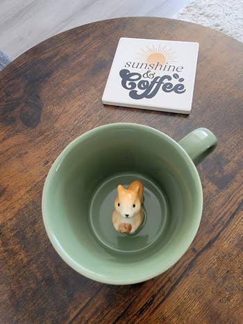 A green cup with a ceramic squirrel inside, on a table with a