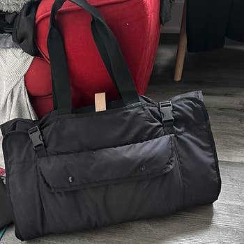 Duffel bag with front pocket and long handles resting on the floor, suggesting practical use for travel or gym essentials