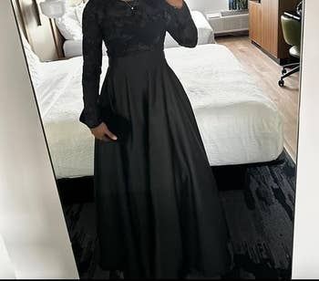 Person in a long, elegant evening gown holding a clutch, stands in a bedroom setting