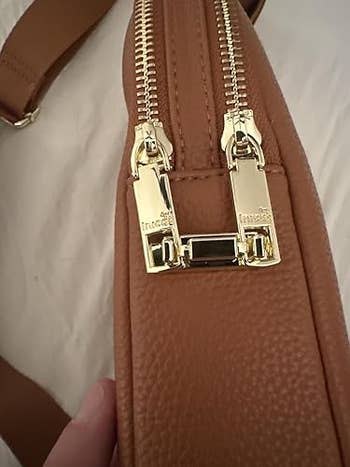 Close-up of a brown leather handbag showcasing its gold zipper and stitching detail