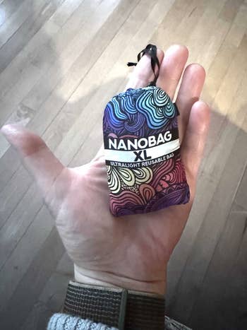 Hand holding a compact Nanobag XL, labeled as an ultralight reusable bag with a colorful pattern