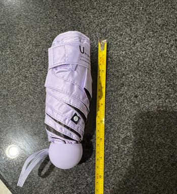 Closed compact umbrella next to a yellow measuring tape on a dark countertop