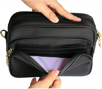 Hands holding a black multi-pocket crossbody bag with a zippered compartment, ideal for shopping or travel
