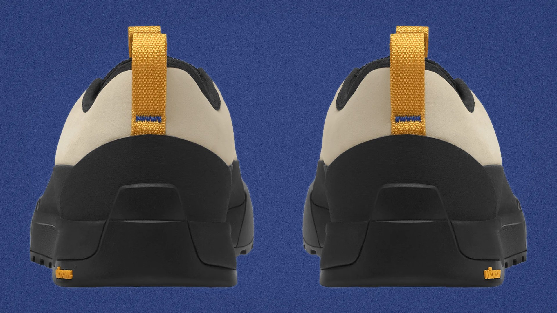 Rear view of beige and black shoes with yellow pull tabs and Vibram logo on the sole against a blue background.
