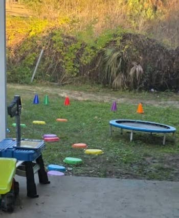 Backyard setup for kids with stepping stones, a small trampoline, and traffic cones surrounded by trees