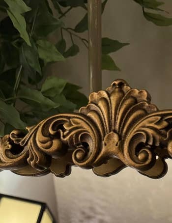 Ornate gold chandelier detail with leafy design, underneath greenery