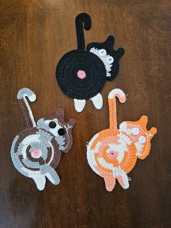 Crocheted cat coasters with humorous spiral designs and button eyes on a wooden surface