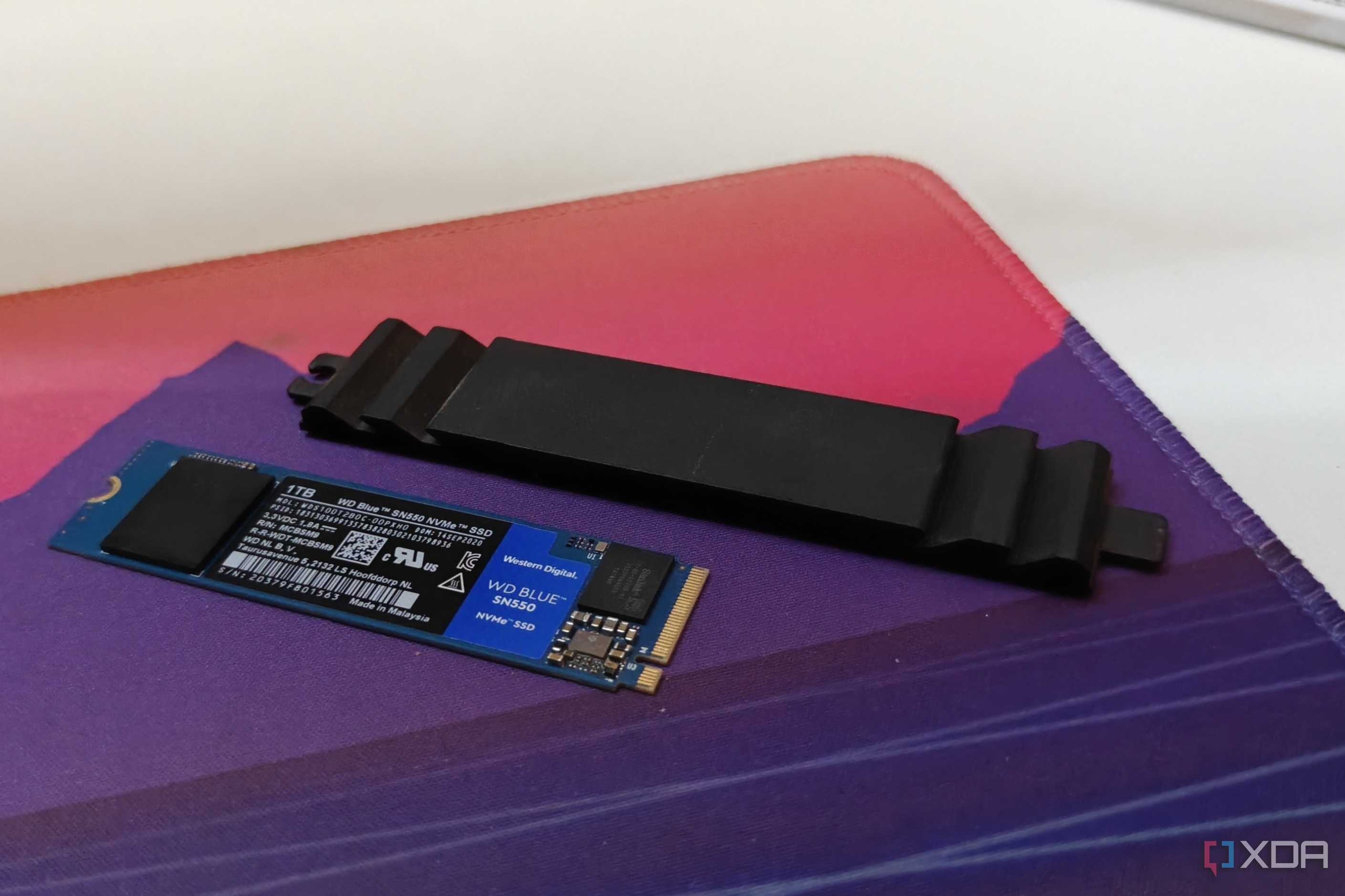 A WD Blue SSD on a deskmat next to a black SSD heatsink
