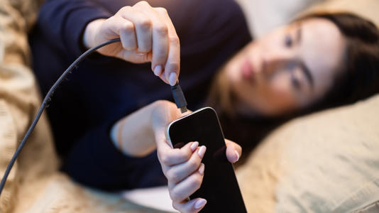 Young woman connecting her phone charger while laying in bed