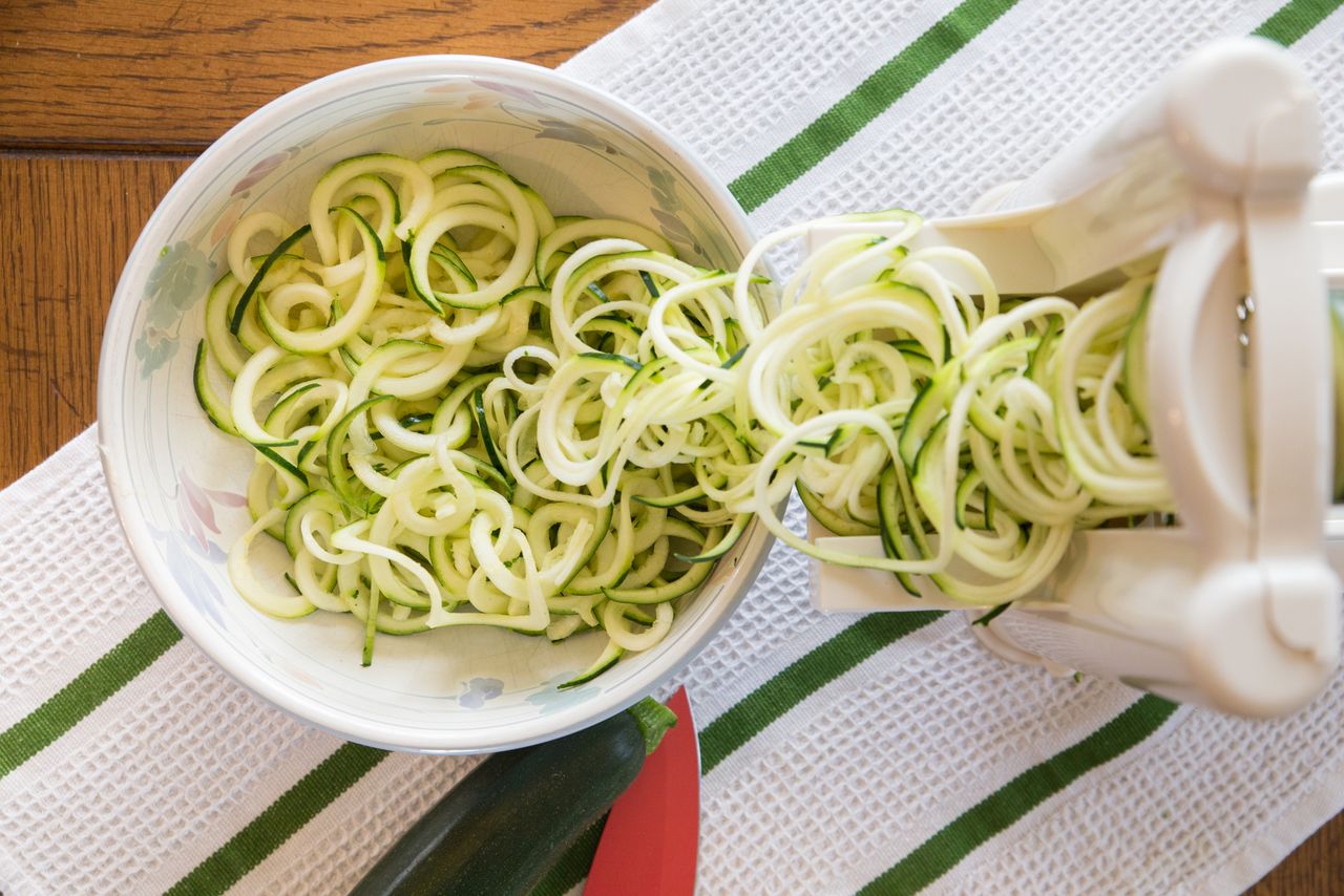 Zucchini noodles being prepared using a spiralizer into a bowl on a kitchen surface