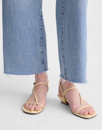 Close-up of a person wearing wide-leg jeans with frayed hems and beige strappy sandals with low heels