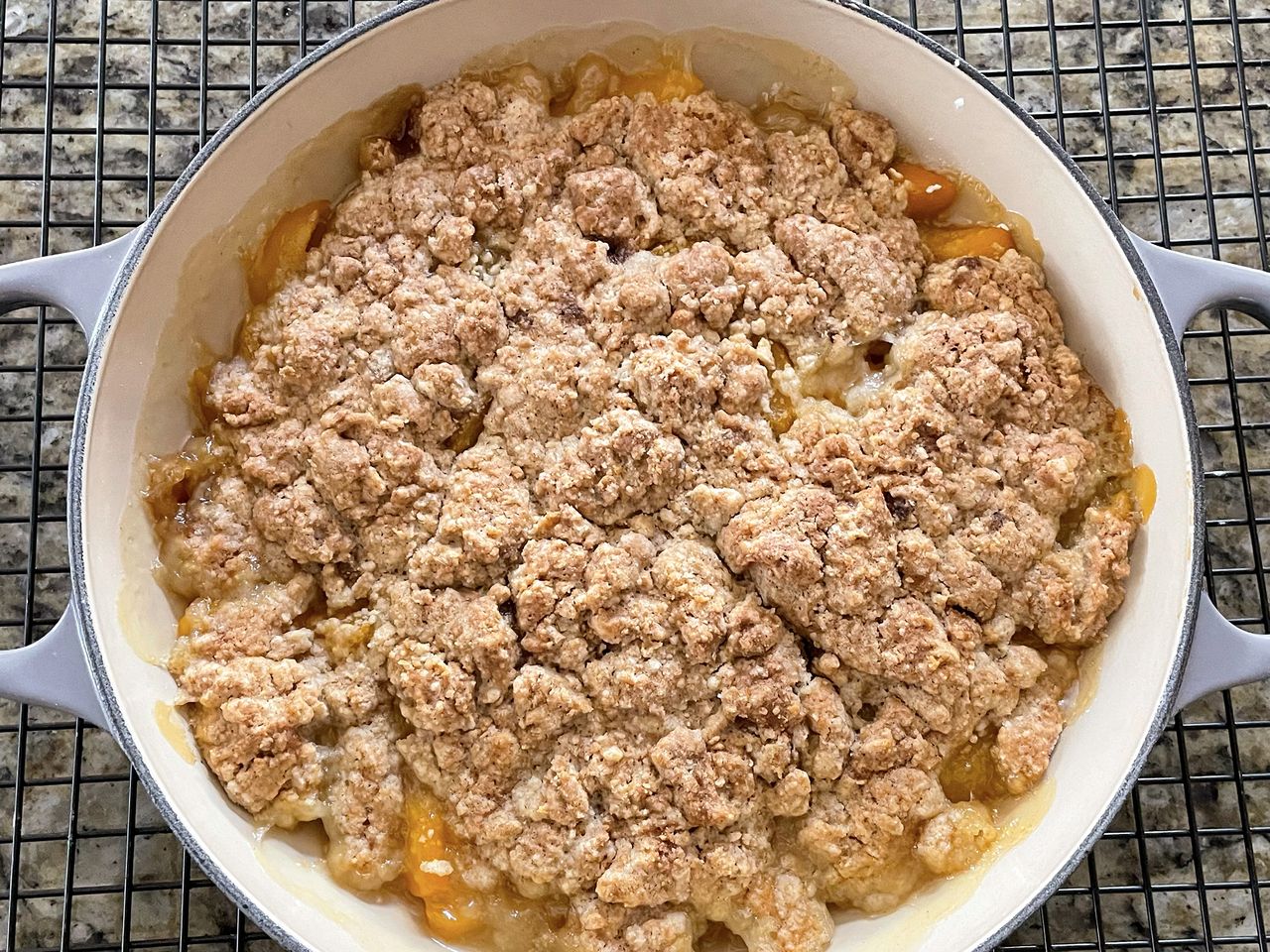 close up view of a Peach Cobbler in a Dutch oven on a cooling rack