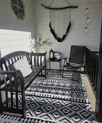 Chic porch setup with black bench, geometric pillow, matching chair, and decorative rug. Ideal for outdoor decor inspiration