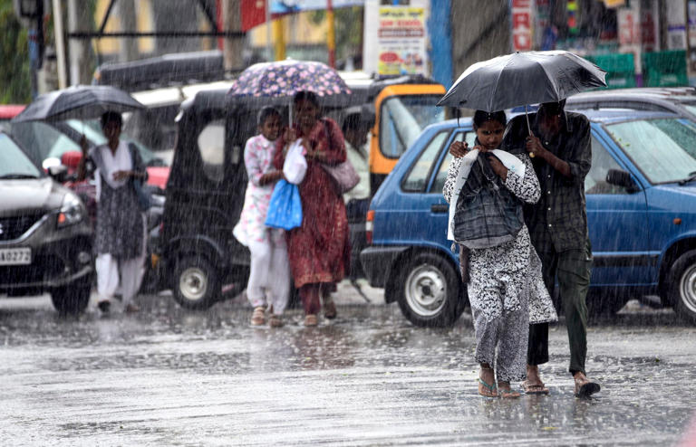 People cover themselves as they walk amid rainfall in Karnataka. (Photo: PTI)