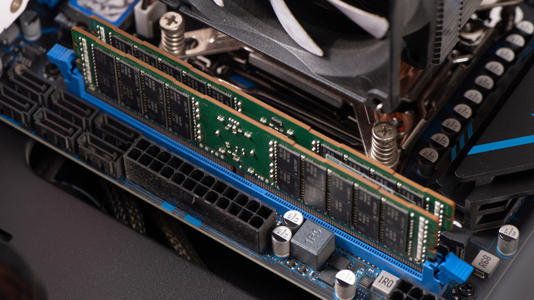 A close-up of a desktop computer motherboard showing installed DDR RAM sticks next to a CPU cooler and the motherboard's 24-pin power connector.