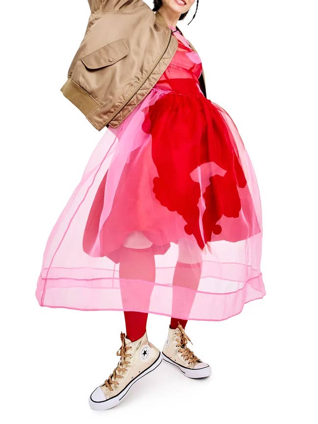 Person wearing a voluminous sheer dress with a bold pattern, paired with a jacket and white sneakers. Fashion-forward ensemble for a shopping feature