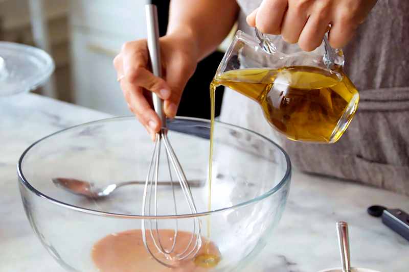 hands whisking olive oil into a bowl of other ingredients to make salad dressing