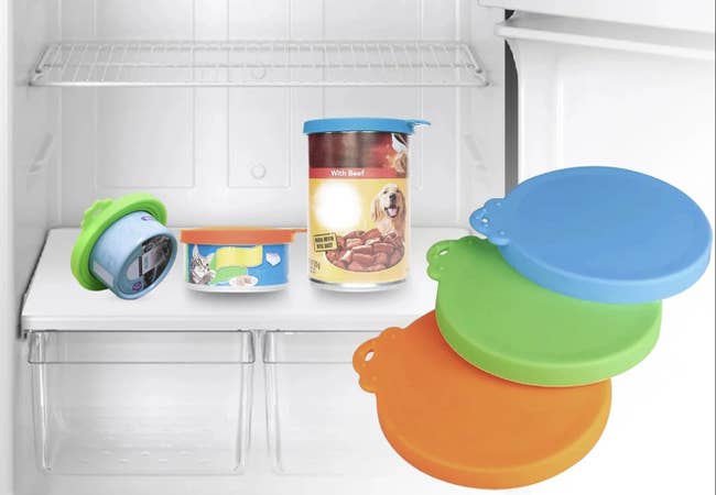 Three pet food cans with colored silicone lids inside a refrigerator. Three additional lids are shown in blue, green, orange