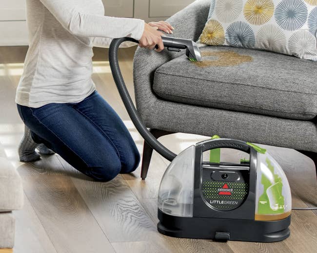Person using a handheld vacuum cleaner to clean a stain on a couch. House is modern and tidy