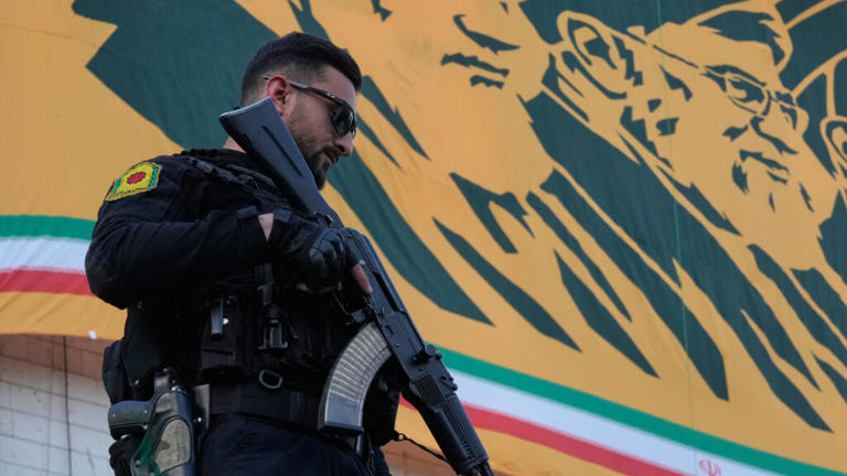 A police officer stands guard near a banner with portraits of former Iranian leaders Ayatollah Khomeini and Ayatollah Ali Khamenei in Tehran, Iran on April 29, 2026.
