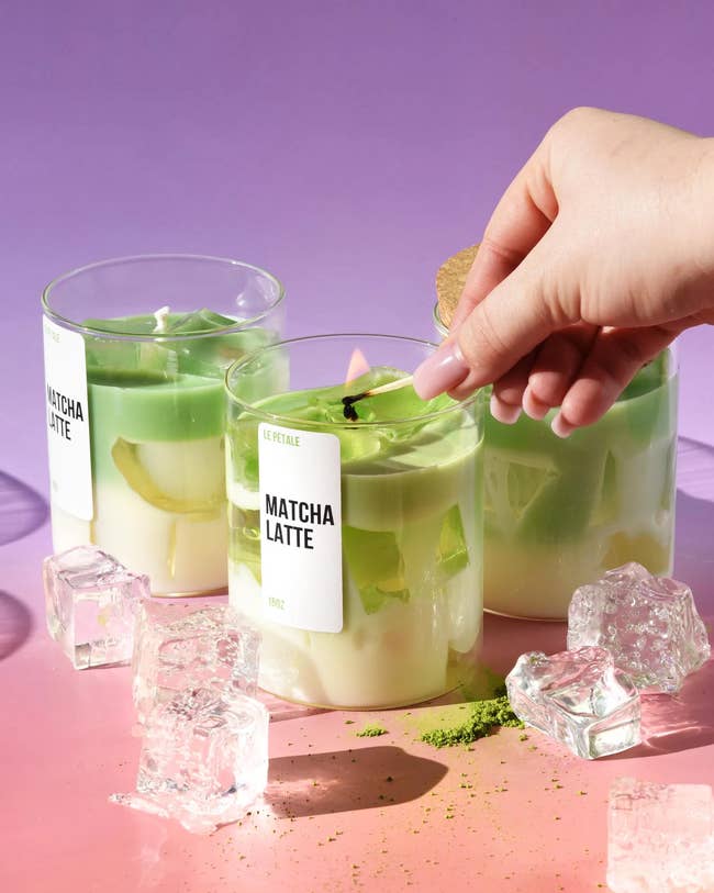 Three glass cups of matcha lattes with ice cubes and a hand placing a leaf garnish