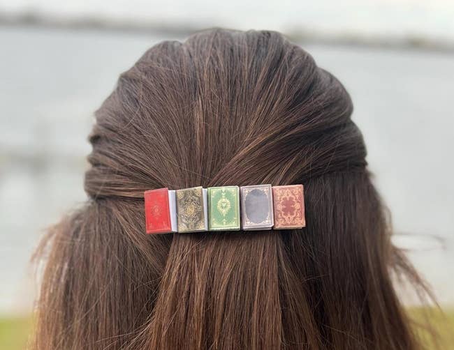 Hairpin styled as vintage books holds hair in a half-updo, outdoor background blurred