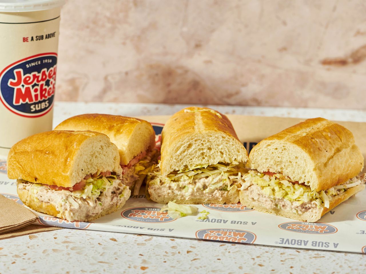 Jersey Mike's tuna sandwiches on branded paper with logo cup.