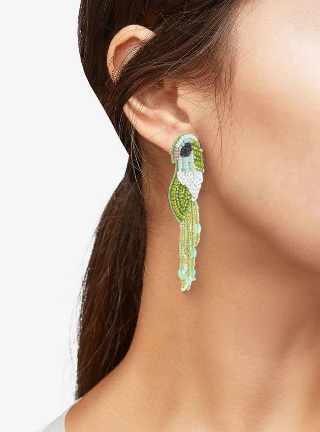 Person wearing long, beaded earrings with intricate parrot design