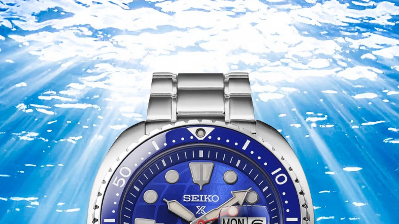 Silver Seiko dive watch with blue bezel and dial, luminescent markers, and day-date display under water.