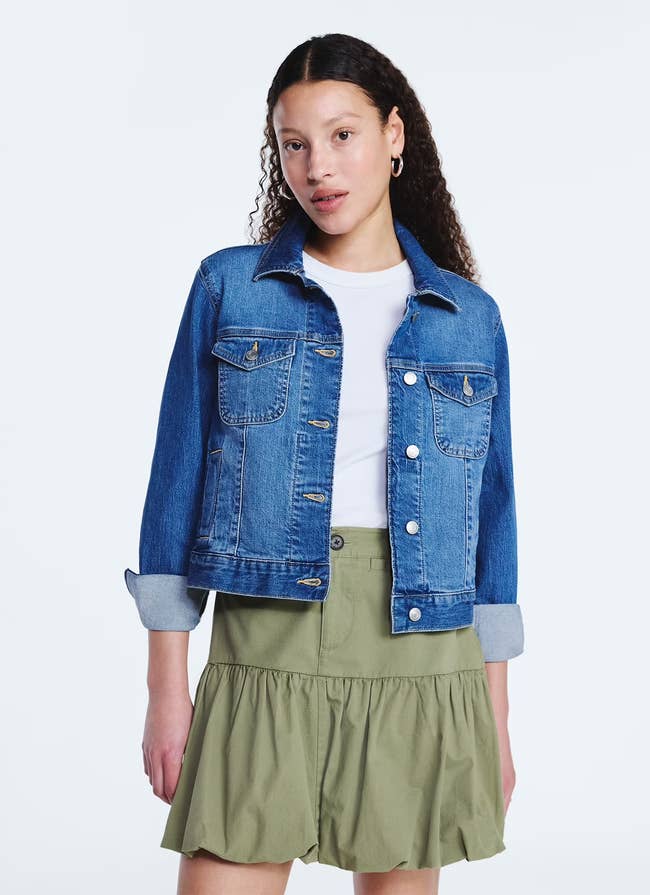Person wearing a denim jacket over a white shirt and a green skirt