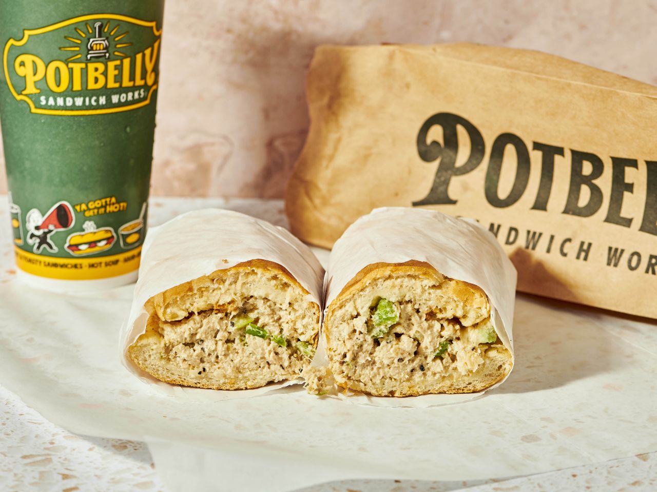 Potbelly tuna sandwich halves with green cup and branded bag.