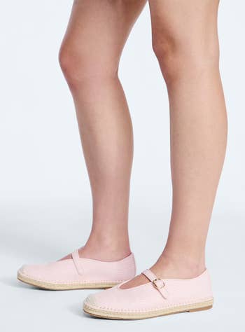 Person wearing light-textured espadrille flats with a strap and buckle detail