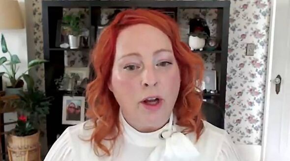 An individual with vibrant red hair, dressed in a white turtleneck, is seated and speaking, with a background featuring a decora