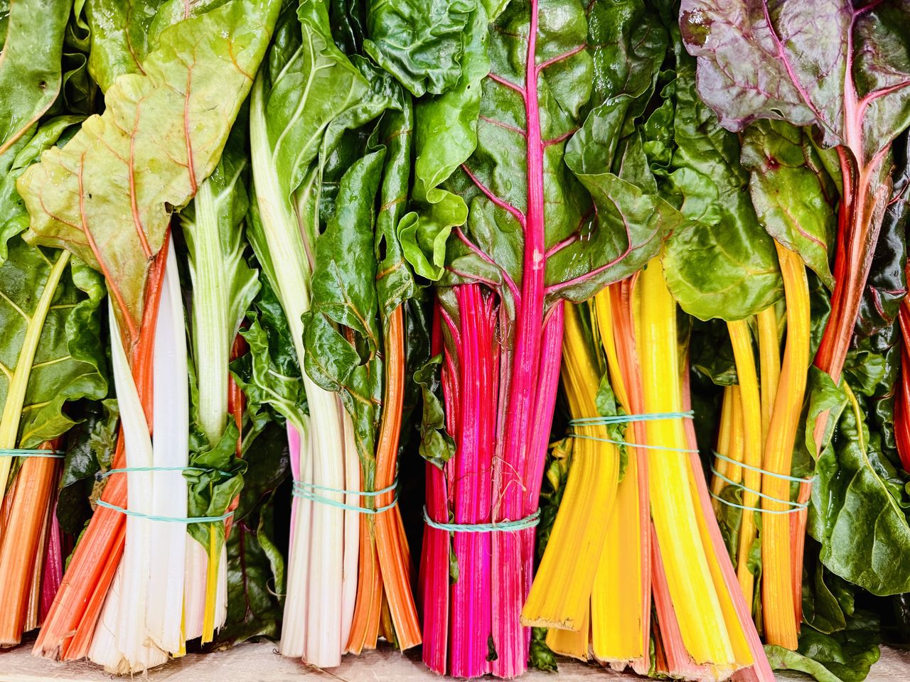 Bundles of leafy vegetables with colorful stems on display