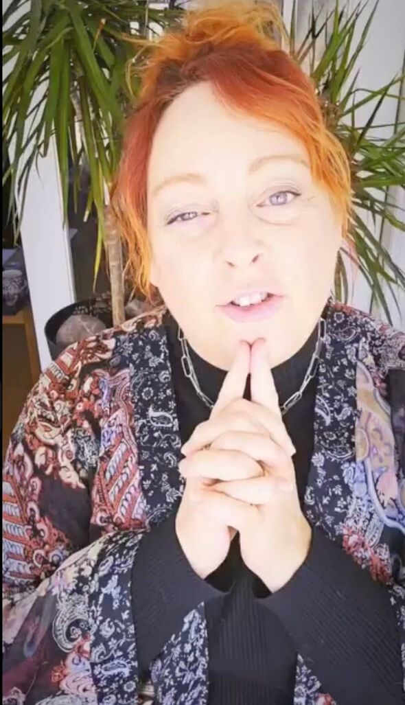 An individual with vibrant red hair and a contemplative expression is seen gesturing with their fingers while addressing the cam