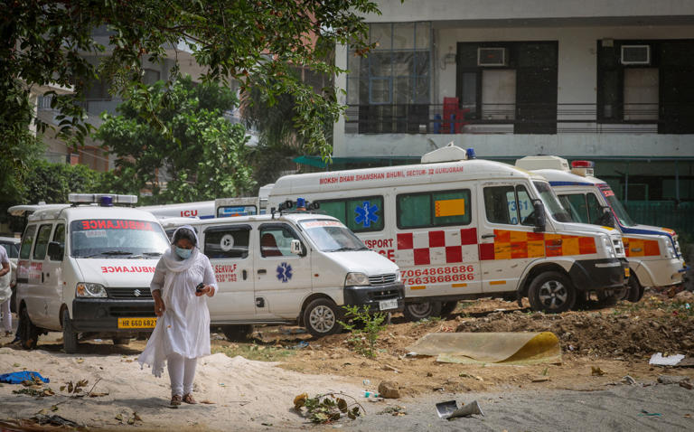 A woman walks past ambulances carrying the remains of Vivek Aggarwal and his family, who died in a fire at a hotel in Delhi on Wednesday, on 4 June 2026 (Reuters)