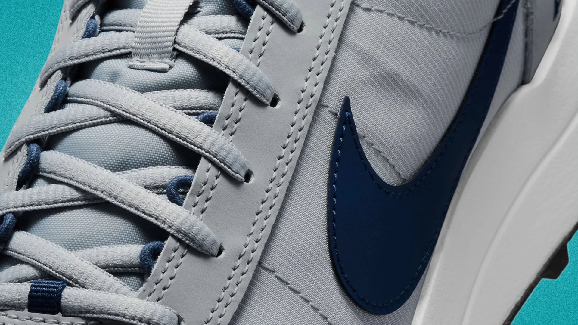 Close-up of light gray sneaker with blue Nike swoosh and matching laces on a teal background.