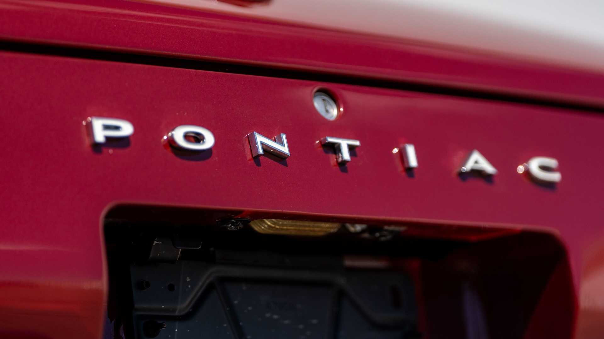 The chrome Pontiac trunk logo on the rear of a red muscle car.