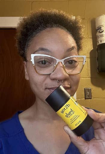 Person holding a container of got2b glued styling product with a smile, standing indoors